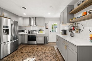 A modern kitchen with stainless steel appliances, white cabinetry, and a patterned rug.
