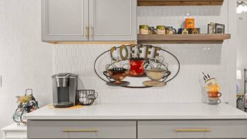 A kitchen with grey cabinets, a coffee station, and a white tiled backsplash.