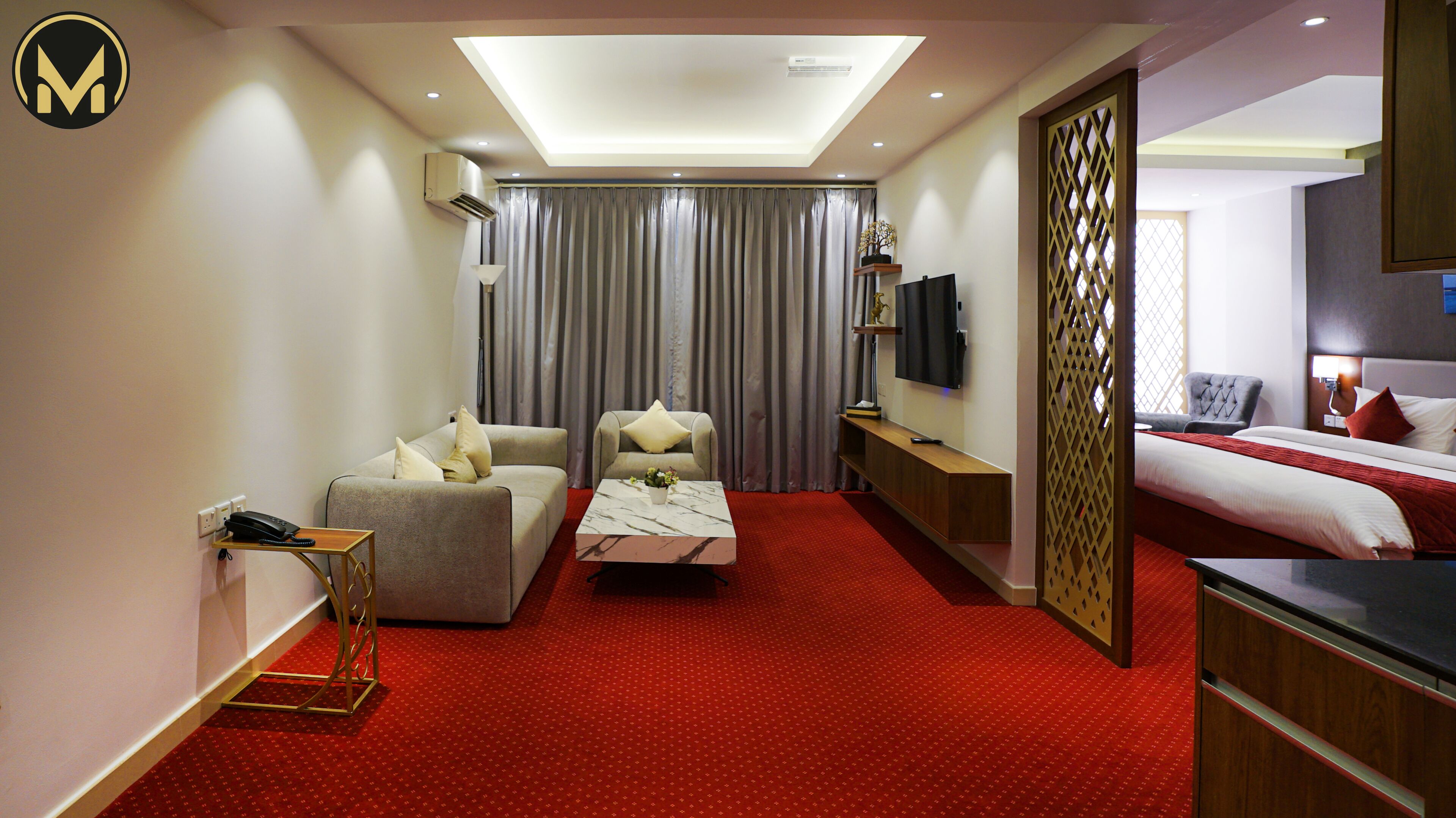 Habitación de hotel con sofá, sillón, una pequeña mesa con un florero, cama, televisor y un separador decorativo.