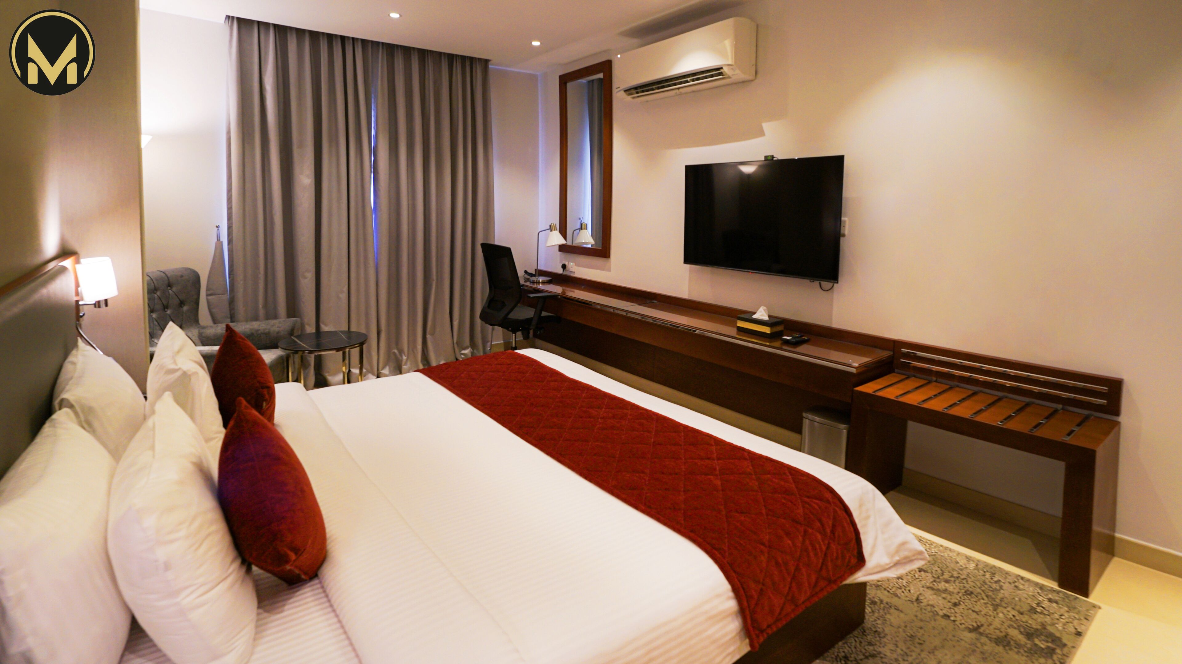 A hotel room with a large bed, a desk, a chair, a television, and a window with curtains.