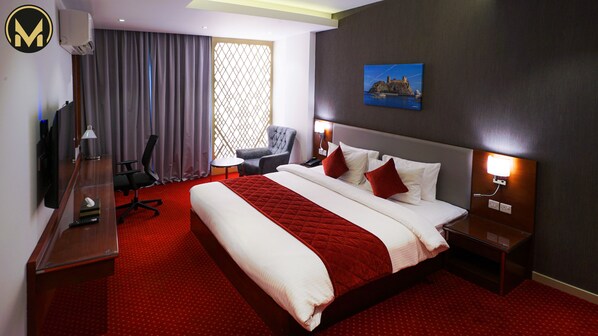 A hotel room with a large bed, a desk, a chair, a TV, and a painting on the wall. - Muscat Express Hotel (Muscat)