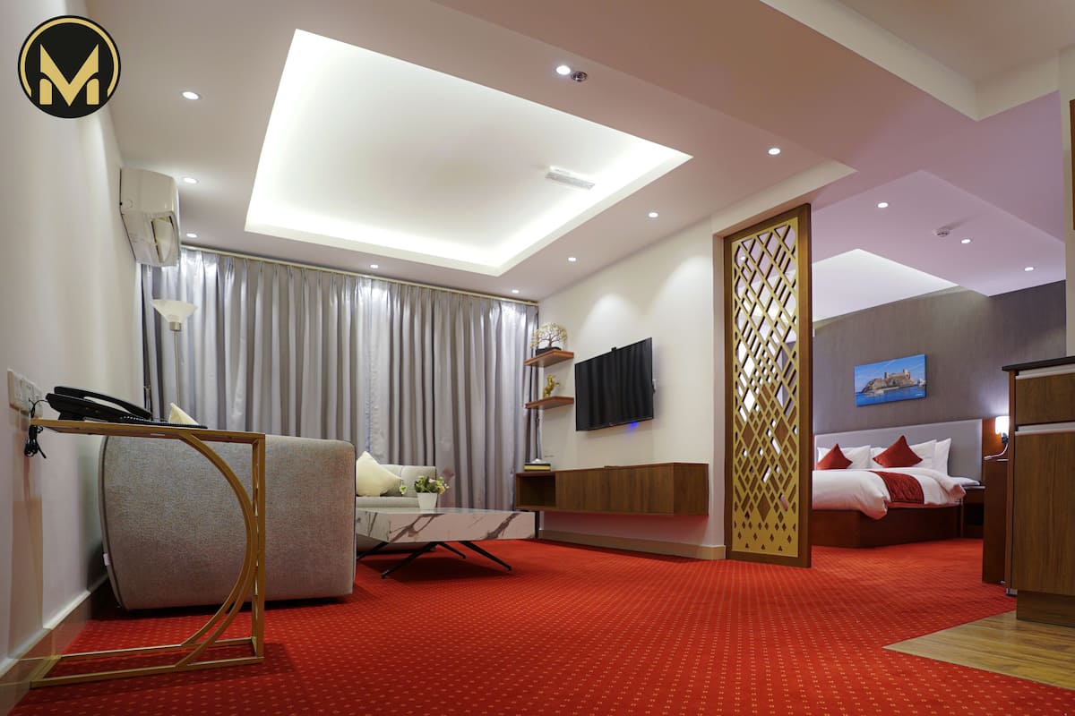 Una habitación de hotel moderna con alfombra roja, un sofá, una cama con almohadas rojas, un televisor y un mueble de madera.