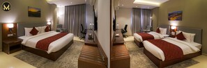 Two large beds with red quilts and white linens, a desk area, flat-screen TV, and armchair.