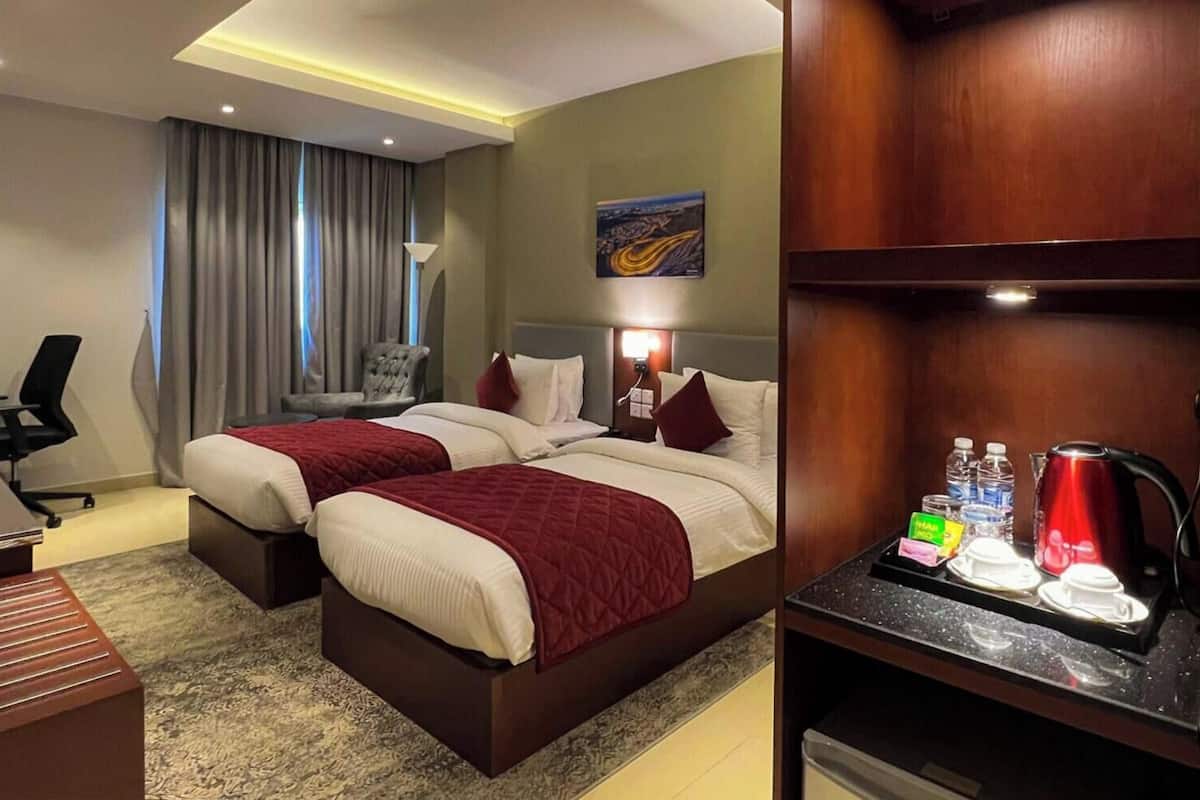 Habitación de hotel con dos camas, un escritorio, una silla, una mesita de noche, un cuadro y una cafetera.