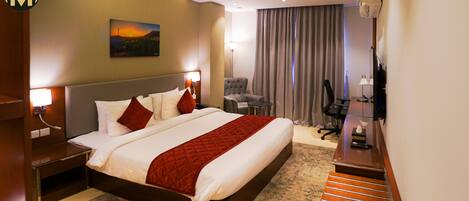 A hotel room with a large bed, a desk, a chair, a lamp, a painting, and a view of the outdoors.