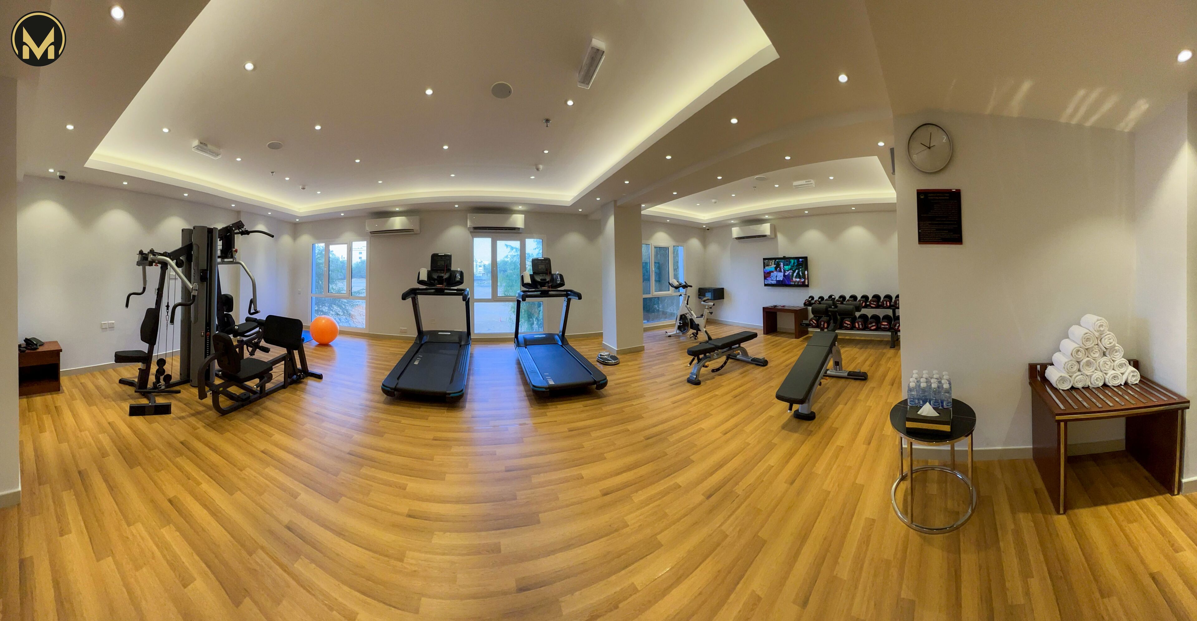 Un gimnasio espacioso con cintas de correr, máquinas de pesas y un banco.