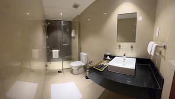 Un baño moderno con ducha de vidrio, inodoro blanco, lavamanos con encimera negra y un espejo sobre el lavamanos.