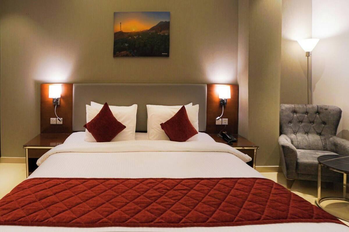 Habitación de hotel con una cama grande, dos lámparas de noche, una silla y un cuadro en la pared.