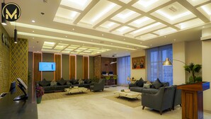 A modern hotel lobby with a reception desk, seating area, and a large screen displaying information. - Muscat Express Hotel (Muscat)