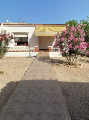 A house with a tiled roof, a front porch with a yellow awning, and a pathway leading to the entrance.