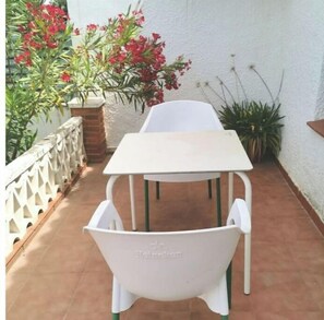 Eine Terrasse mit einem weißen Tisch und zwei weißen Stühlen, umgeben von Kübelpflanzen und einer weißen Mauer.