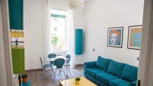 Un salon moderne avec un canapé de couleur turquoise, une table basse jaune et un coin repas comprenant une table et des chaises en verre.