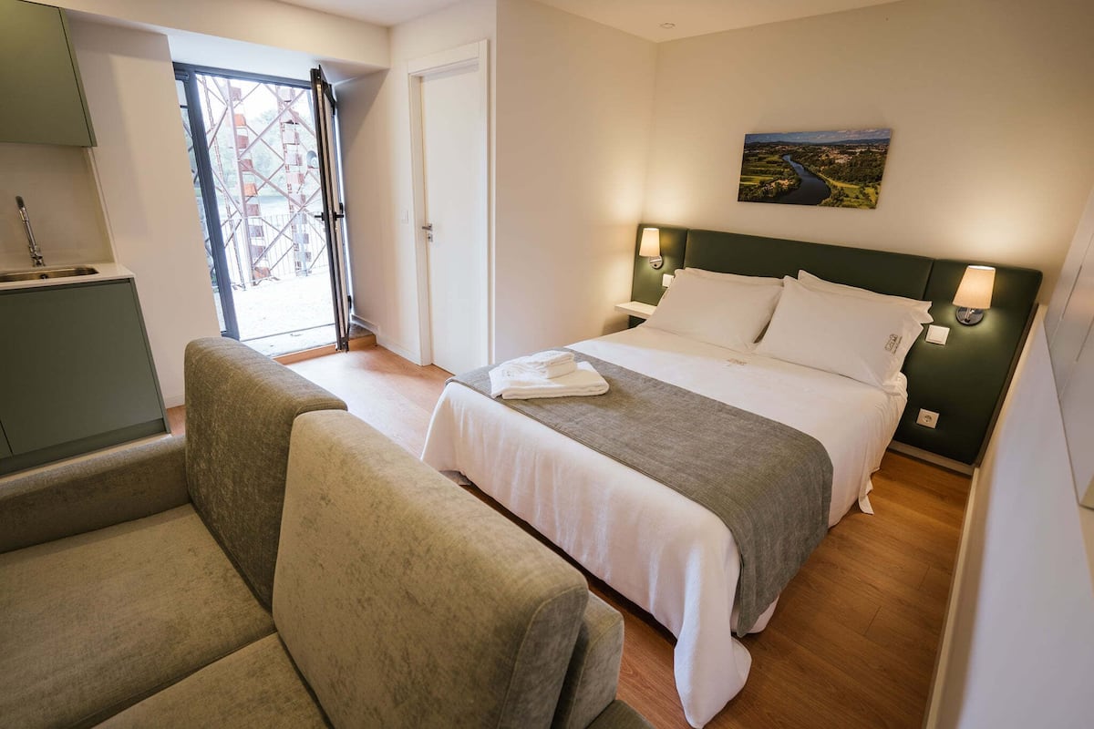 A hotel room with a bed, a sofa, a desk, and a view of a river through a window.