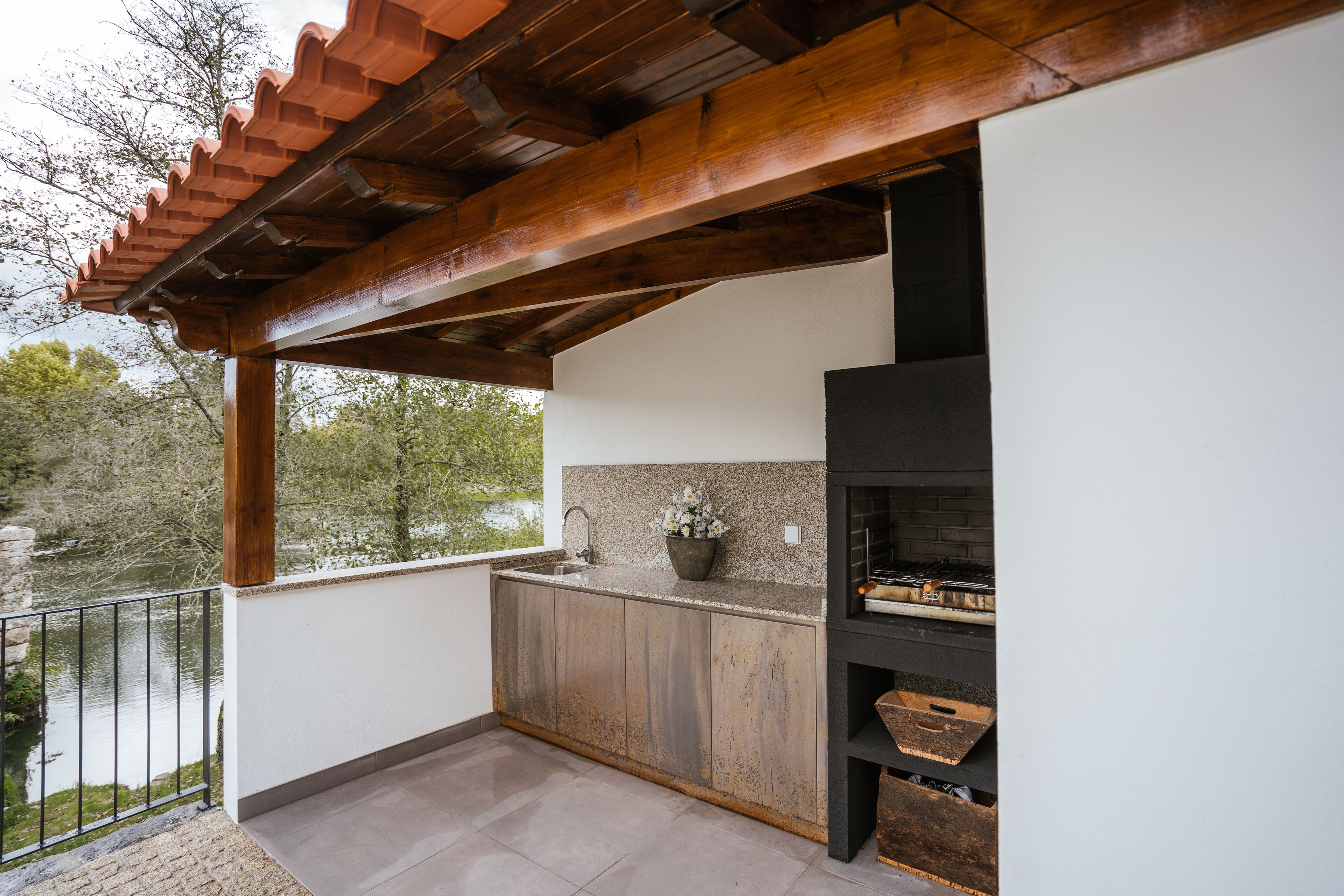 A covered outdoor kitchen with a stone backsplash, wooden cabinets, and a black grill.