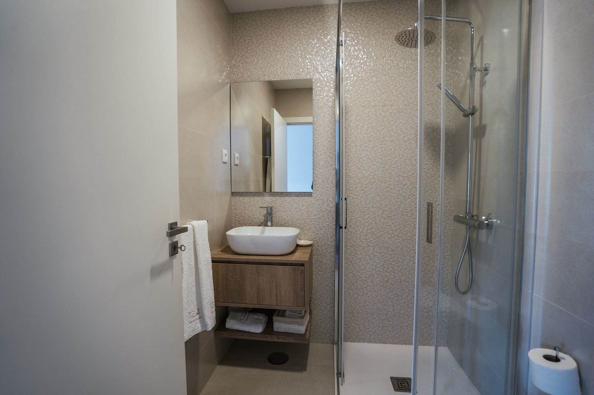 Ein modernes Badezimmer mit Duschkabine aus Glas, einem weißen Waschbecken und einem hölzernen Waschtisch.