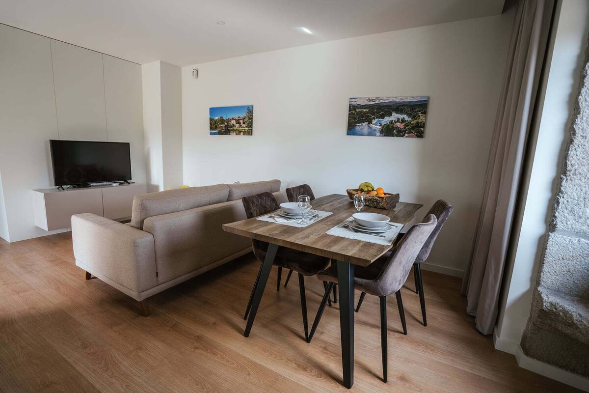 A modern living room with a sofa, a dining table set for two, and a flat-screen TV mounted on a cabinet.