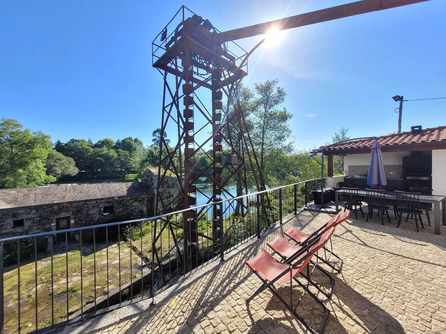 A rustic outdoor area with a metal structure, stone walls, and a view of a body of water.