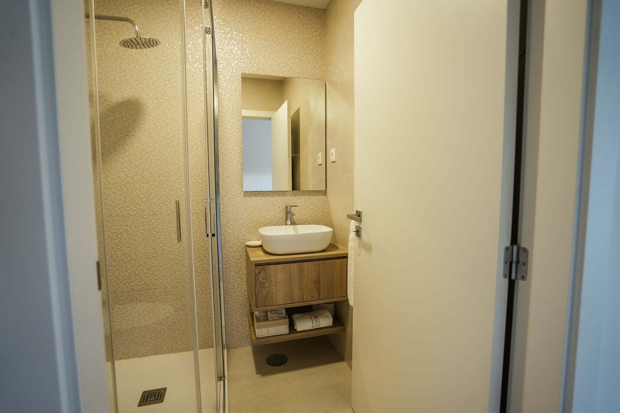 Een badkamer met een douchecabine van glas, een wastafel met een houten meubel eronder, en een spiegel boven het meubel.
