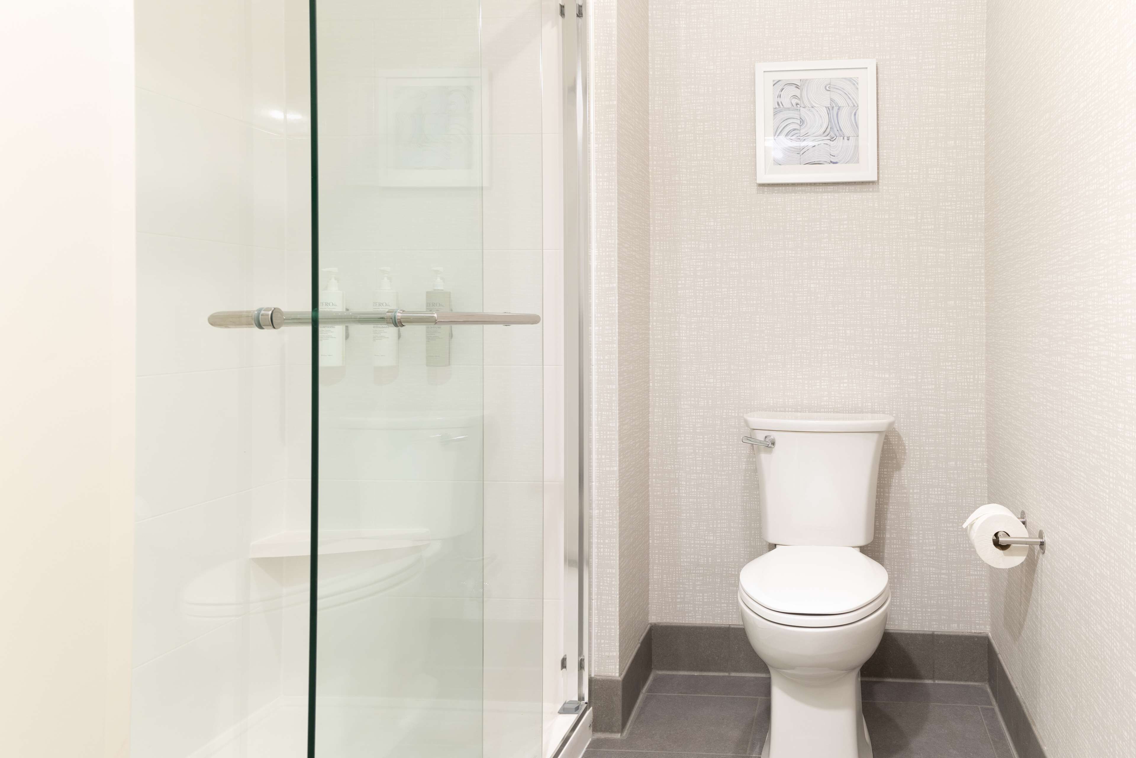 A bathroom with a glass shower enclosure, a toilet, and a framed artwork on the wall.