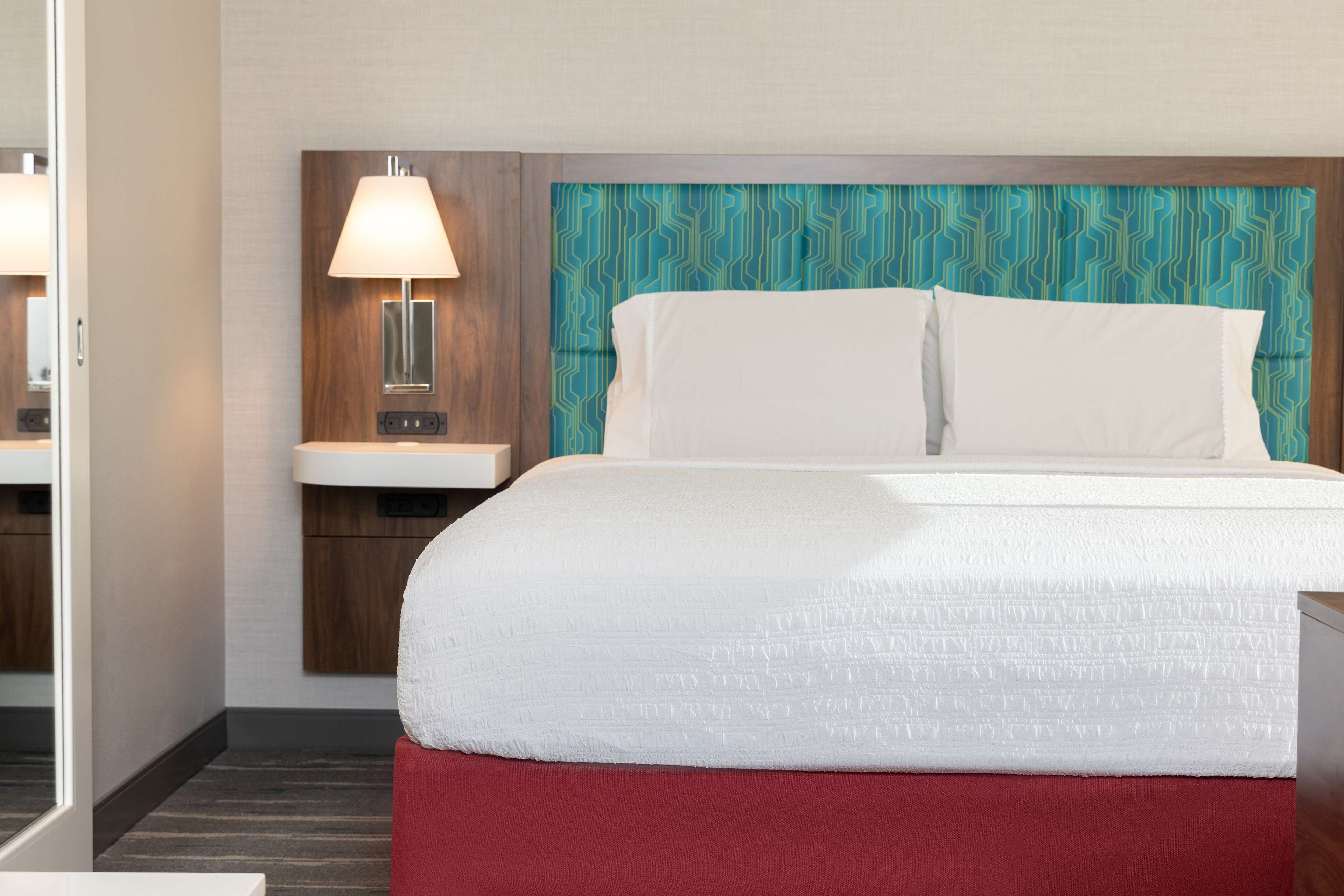 A hotel room with a bed, a nightstand with a lamp, and a patterned headboard.