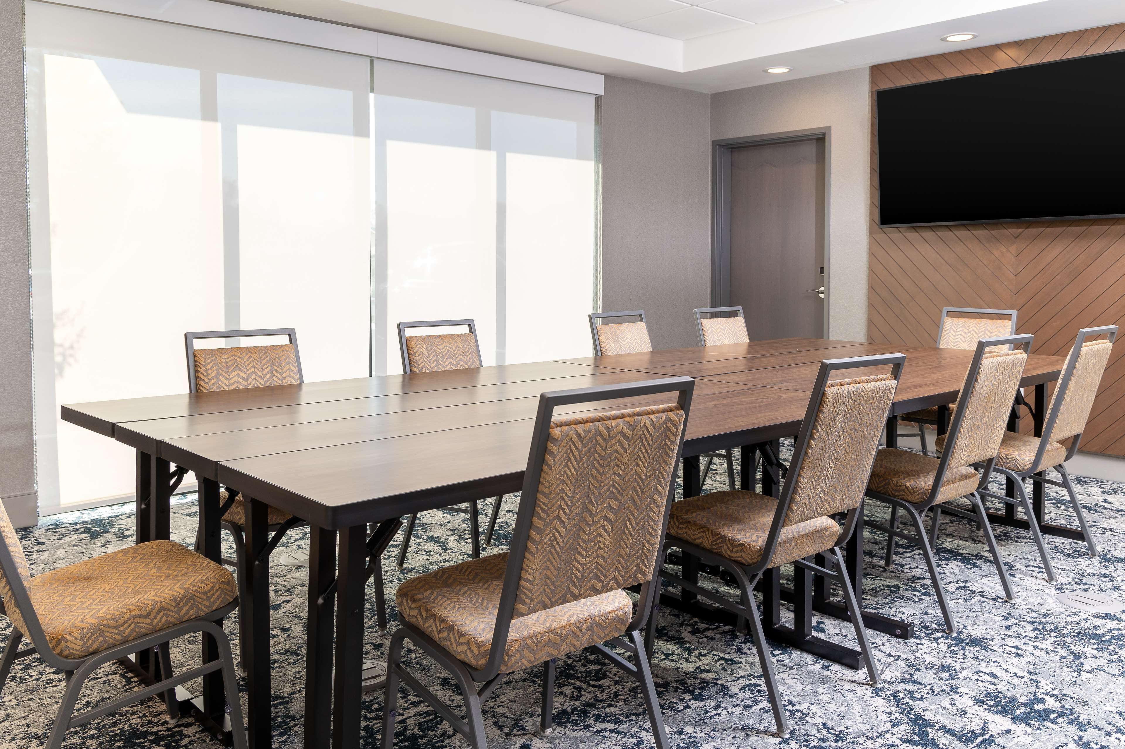 A conference room with a large table and eight chairs, large windows, and a wall-mounted TV.
