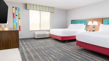 Habitación de hotel con dos camas, televisión, ventana con cortinas a rayas y suelo alfombrado.