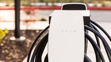 A Tesla electric vehicle charging station with a white charging unit and multiple black cables.