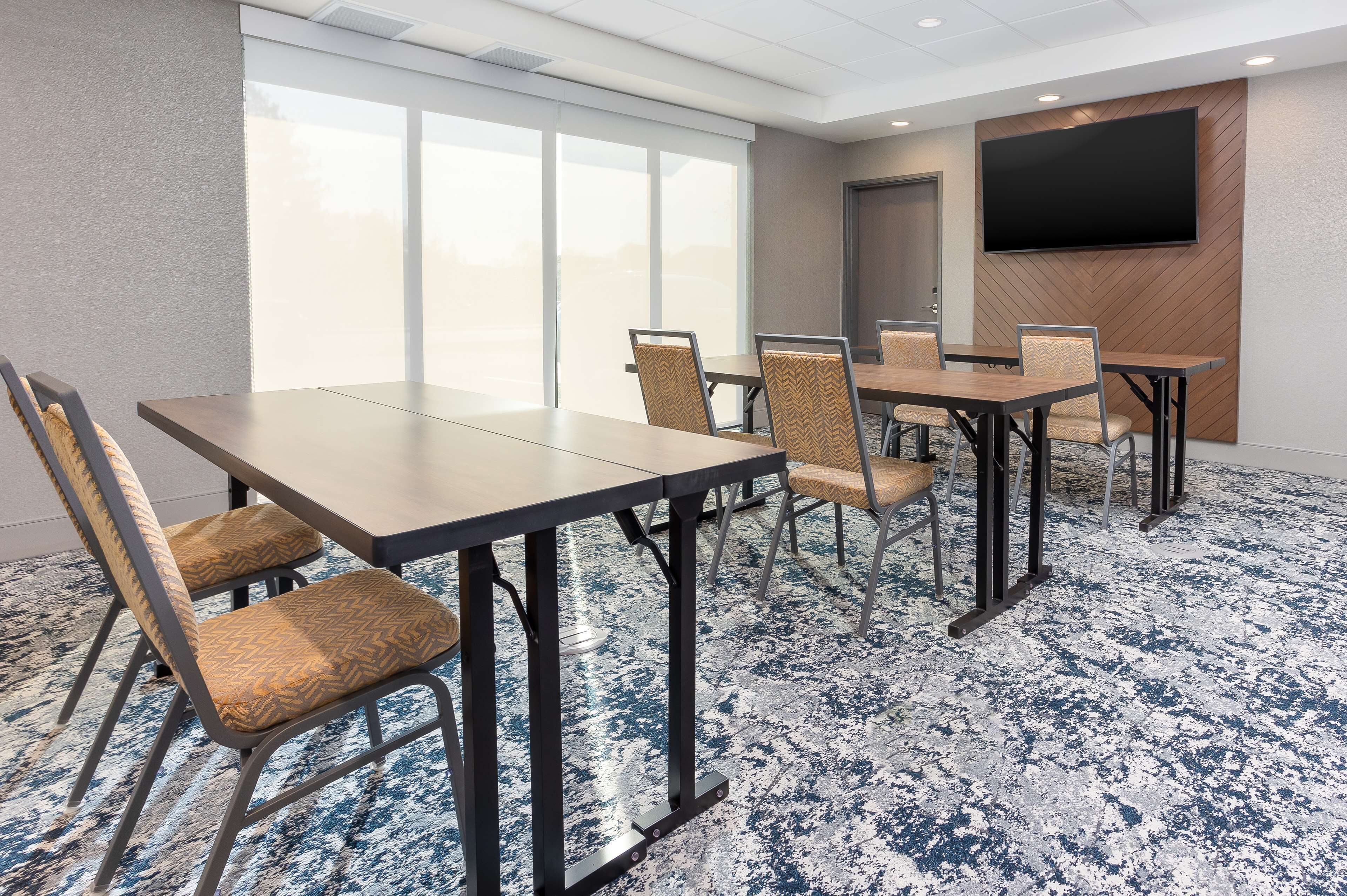 A conference room with a large table, six chairs, a flat-screen TV, and large windows.