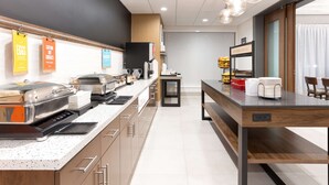 A modern kitchen with a long counter, coffee machines, and a coffee station.
