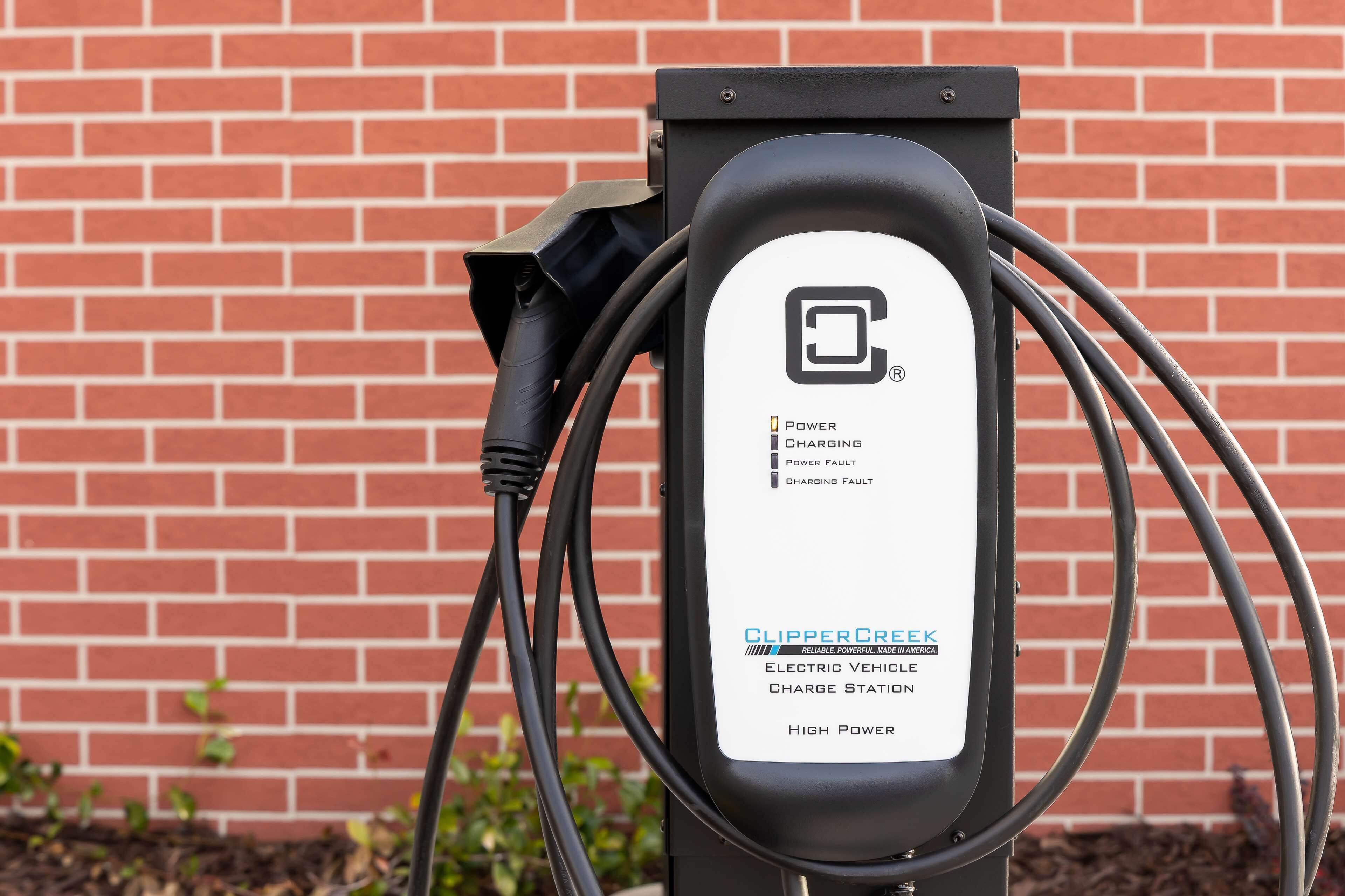 Una estación de carga para vehículos eléctricos ClipperCreek con un muro de ladrillos de fondo.