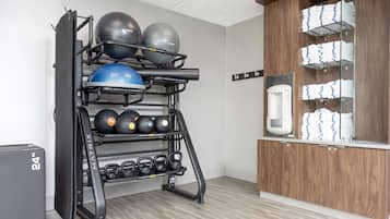 A gym with a wall-mounted rack holding various exercise balls and weights, a water dispenser, and neatly stacked towels.