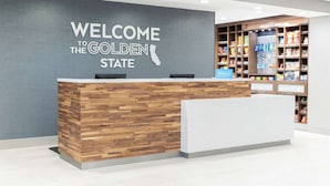 En reception med træ- og hvid design, et skilt på væggen med teksten "WELCOME TO THE GOLDEN STATE" og et udvalg af snacks og drikkevarer.