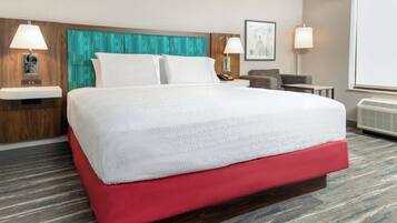 A hotel room with a large bed, a red upholstered headboard, two bedside tables with lamps, a small desk, and a large window.