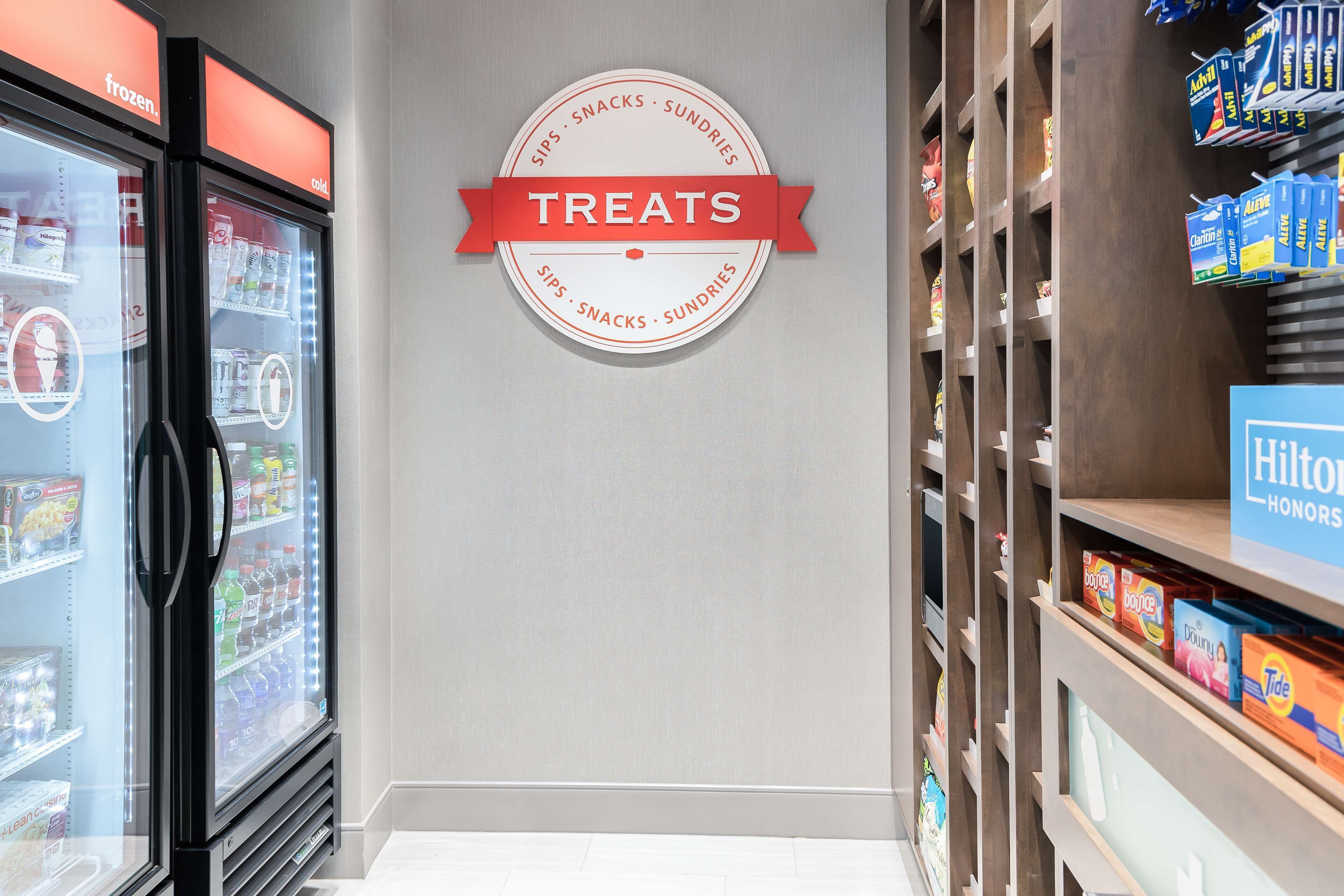 A hotel corridor with a wall sign labeled "TREATS" and shelves stocked with toiletries and snacks.
