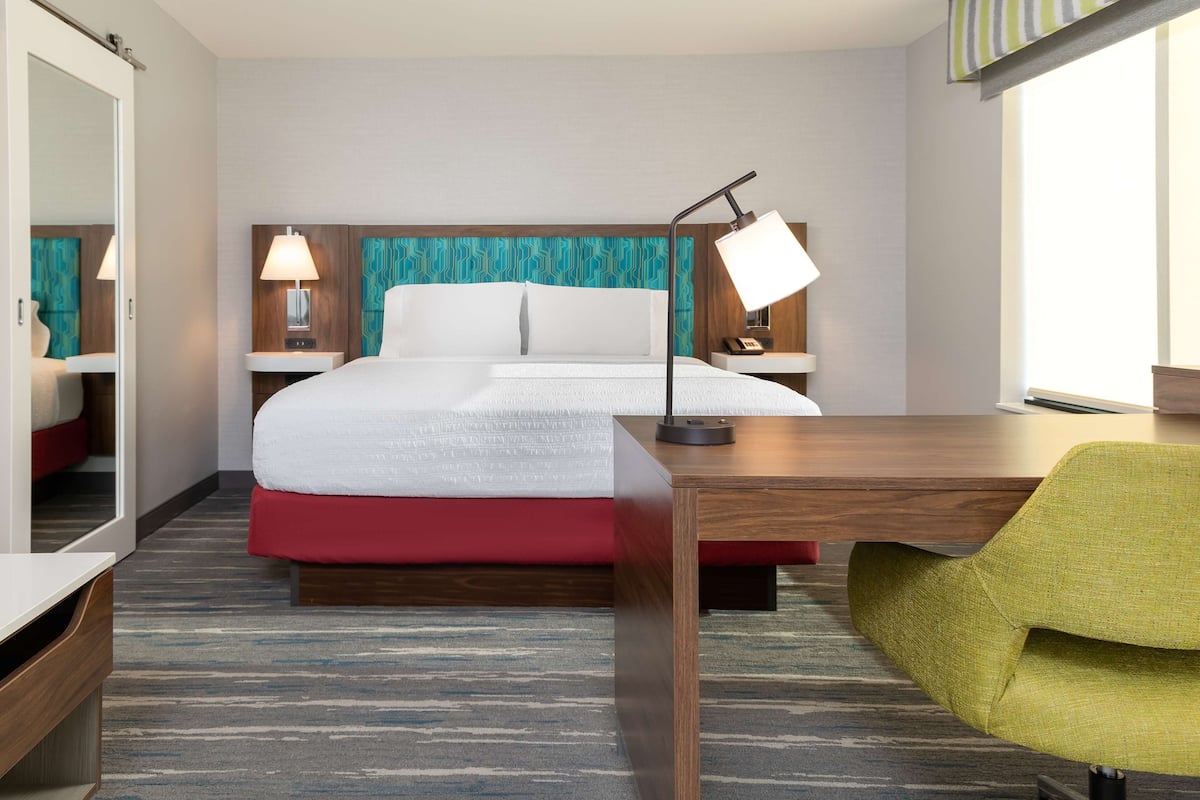 A hotel room with a bed, bedside lamps, a desk, a chair, and a large mirror.