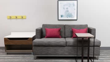 A modern living room with a grey sofa, two red cushions, a small side table, and a framed abstract painting on the wall.