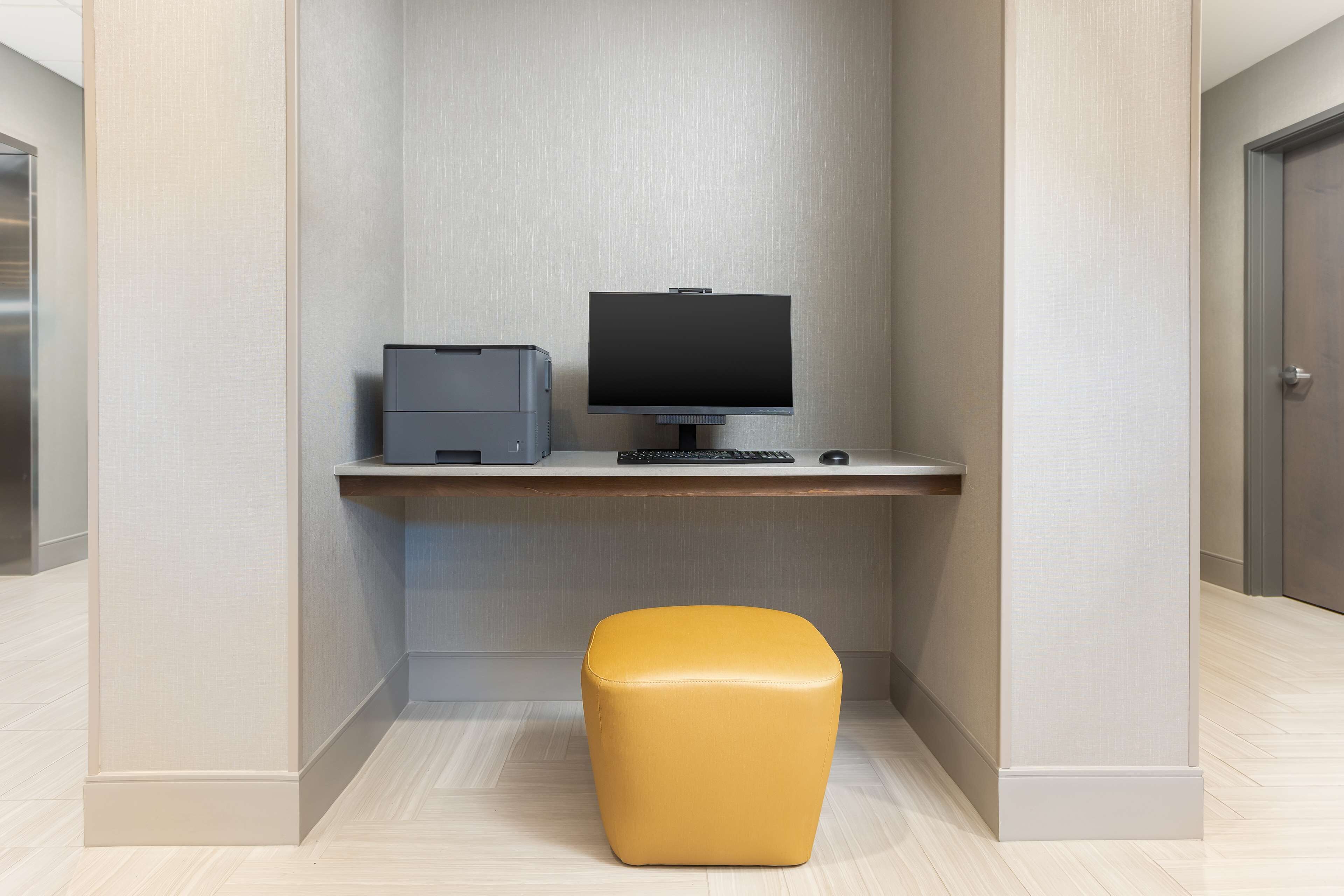 A modern office space with a desk, computer, printer, and a yellow ottoman.