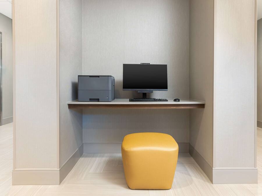 A modern office space with a desk, computer, printer, and a yellow ottoman.