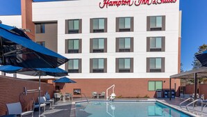 A Hampton Inn & Suites with a pool area, outdoor seating, and a clear blue sky.