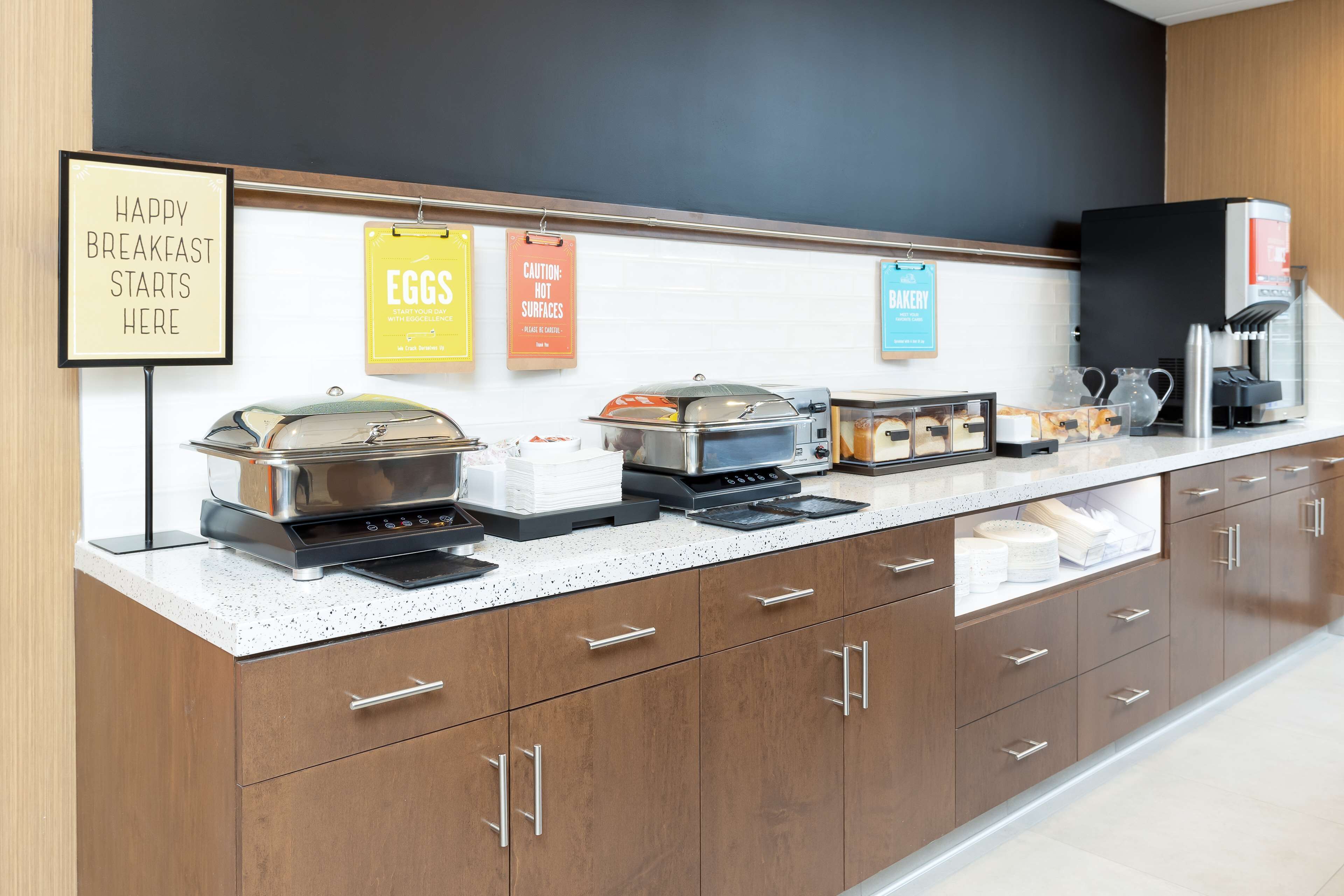 A breakfast bar with various food stations, including a coffee machine and a sign that reads "HAPPY BREAKFAST STARTS HERE".