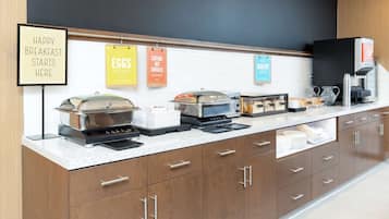 A breakfast bar with various food stations, including a coffee machine and a sign that reads "HAPPY BREAKFAST STARTS HERE".