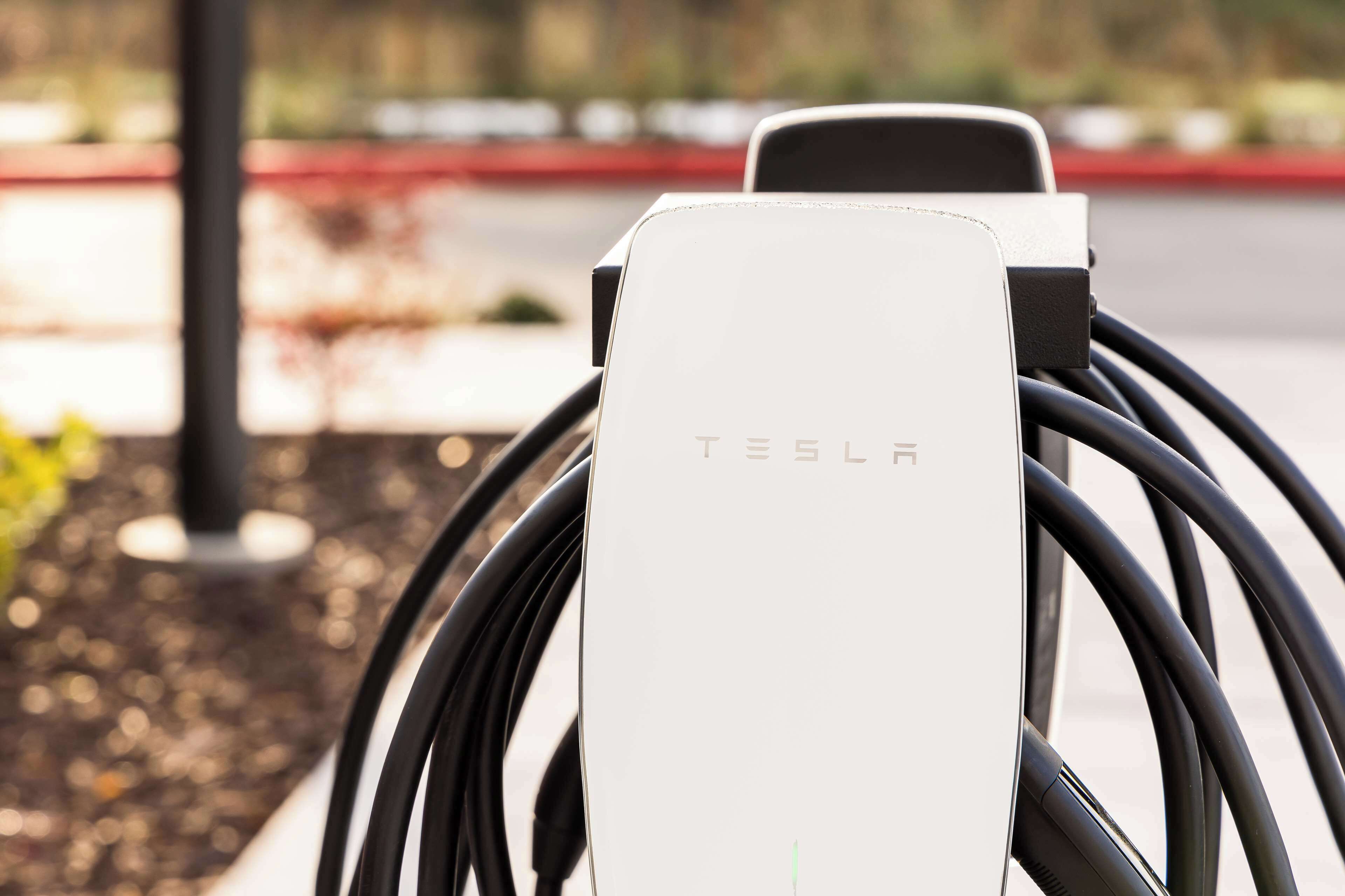 A Tesla charging station with a white charging unit and black cables.