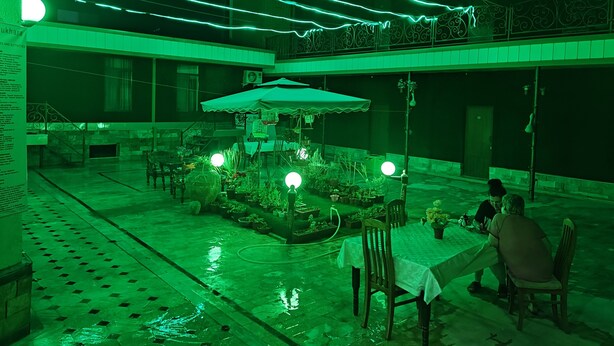 An outdoor dining area with tables and chairs, surrounded by potted plants and a central umbrella. - Green House Hotel (Bukhara)