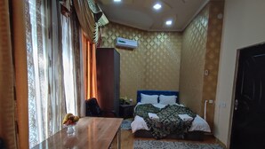 A hotel room with a bed, a desk, a chair, a wardrobe, and an air conditioning unit. - Green House Hotel (Bukhara)