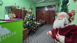 A reception area with a Christmas tree, a desk with a computer, and a person in a Santa costume. - Green House Hotel (Bukhara)