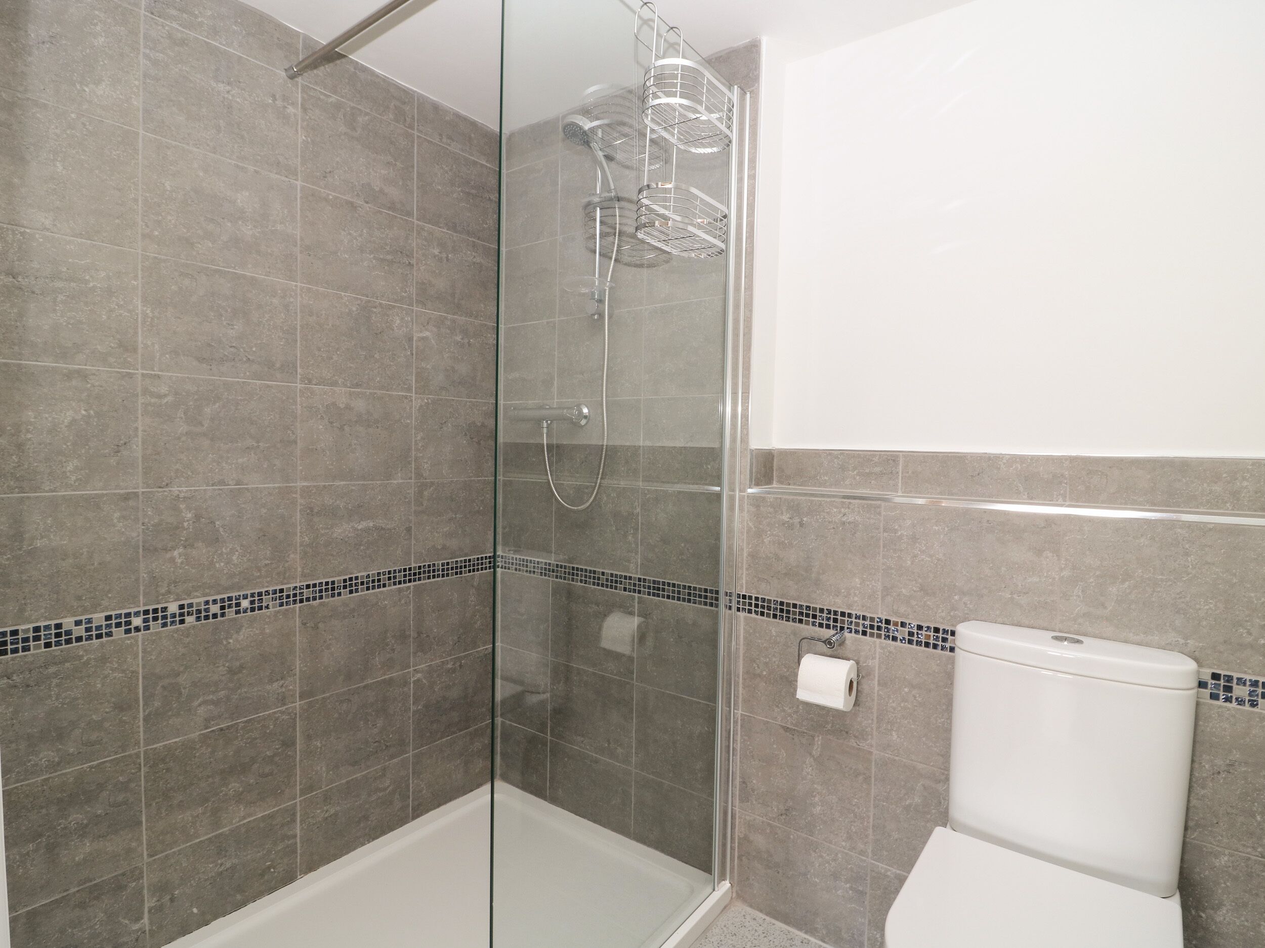 A modern bathroom with a glass-enclosed shower, grey tiles, and a white toilet.