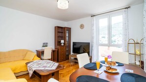 Una sala de estar con sofá, televisor, mesa de comedor y estantería.