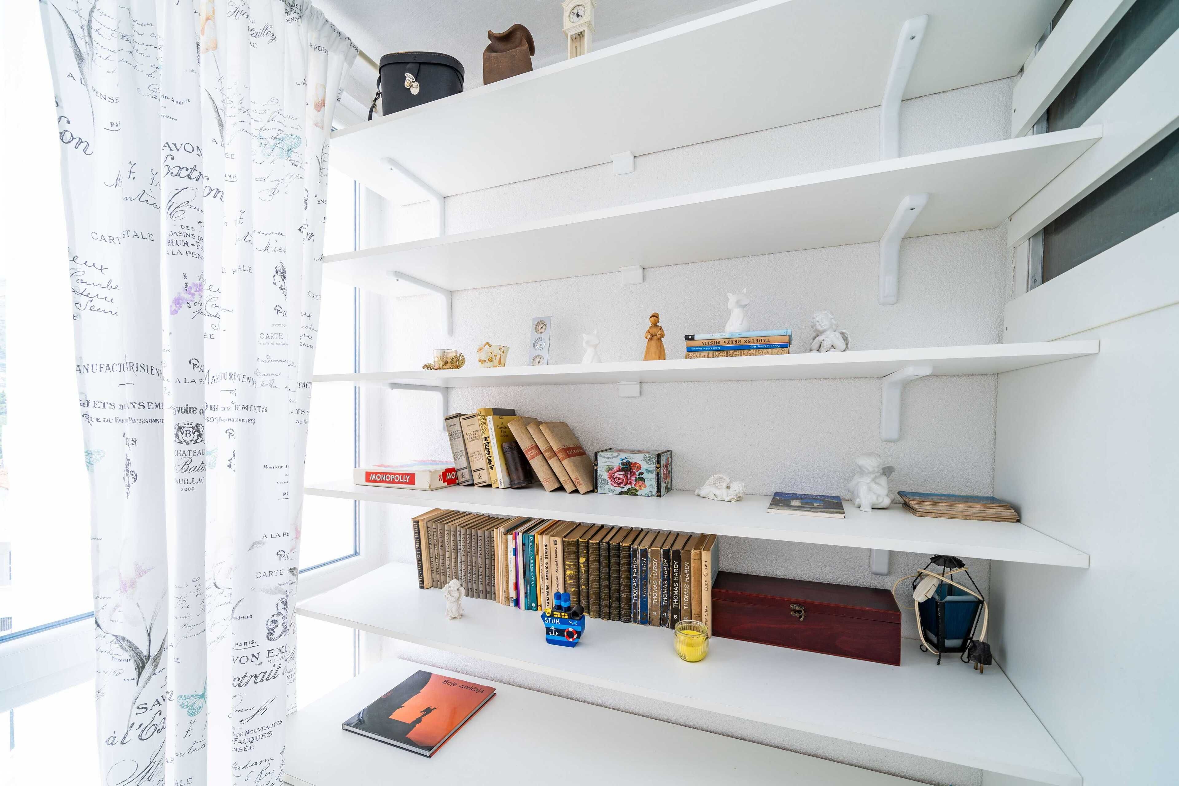Uma estante branca com diversos objetos, incluindo livros, uma pequena estatueta e itens decorativos.