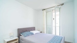 Un dormitorio con cama, mesita de noche y ventana con cortinas.