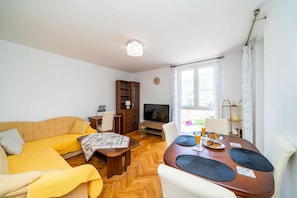 Un salon comprenant un canapé, un téléviseur, une table à manger et une fenêtre avec des rideaux.